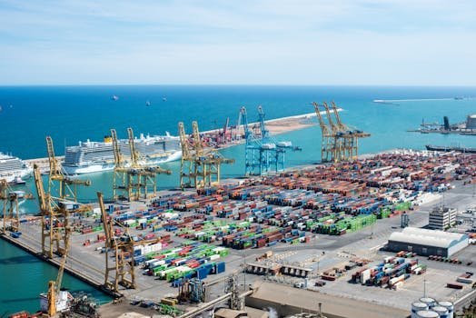 A vibrant aerial shot of Barcelona port featuring cranes, containers, and cruise ships on a sunny day.